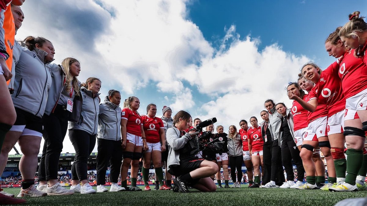 A camera operator kneeling inside a huddle of Wales players and staff at the Arms Park